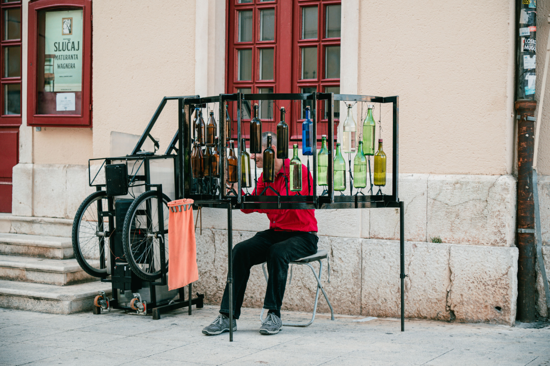 Ljetna atmosfera ispred kazališta uz uličnog svirača koji svira boce