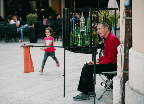 Ljetna atmosfera ispred kazališta uz uličnog svirača koji svira boce